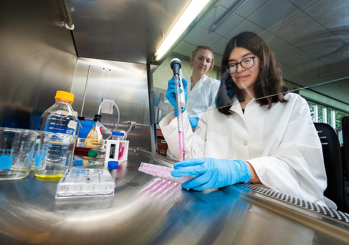 Student working in a lab with a professor looking on from behind